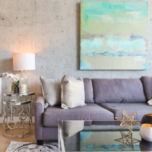 living room with a modern grey couch, coffee table, side table, lamp and art piece over top